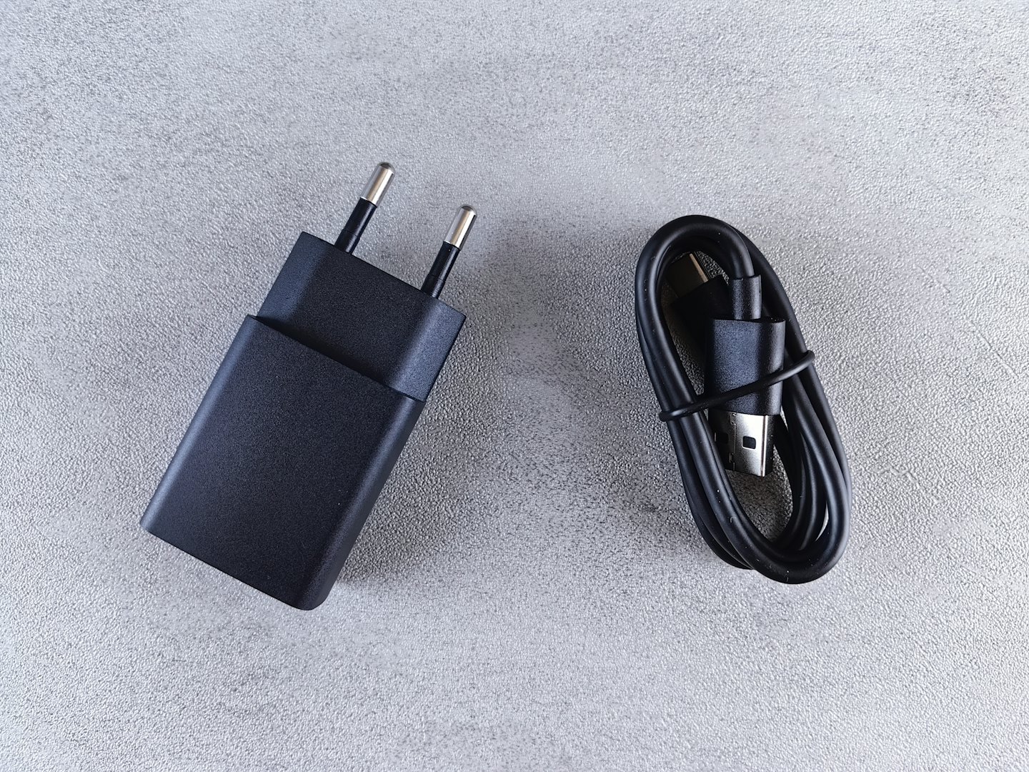 Cargador de teléfono negro y cable enrollado sobre una superficie gris.