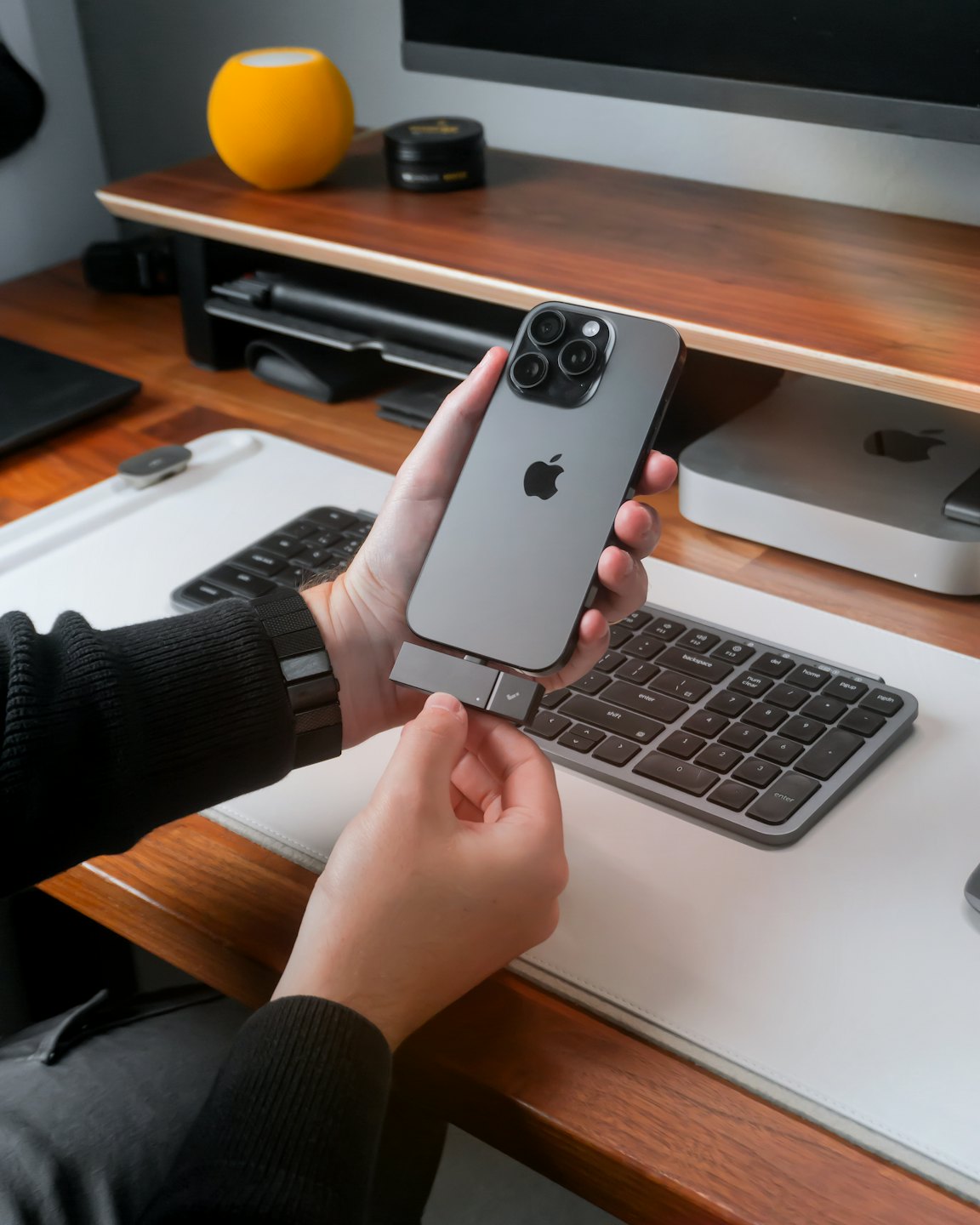 Manos conectando un accesorio a un teléfono inteligente sobre un escritorio.