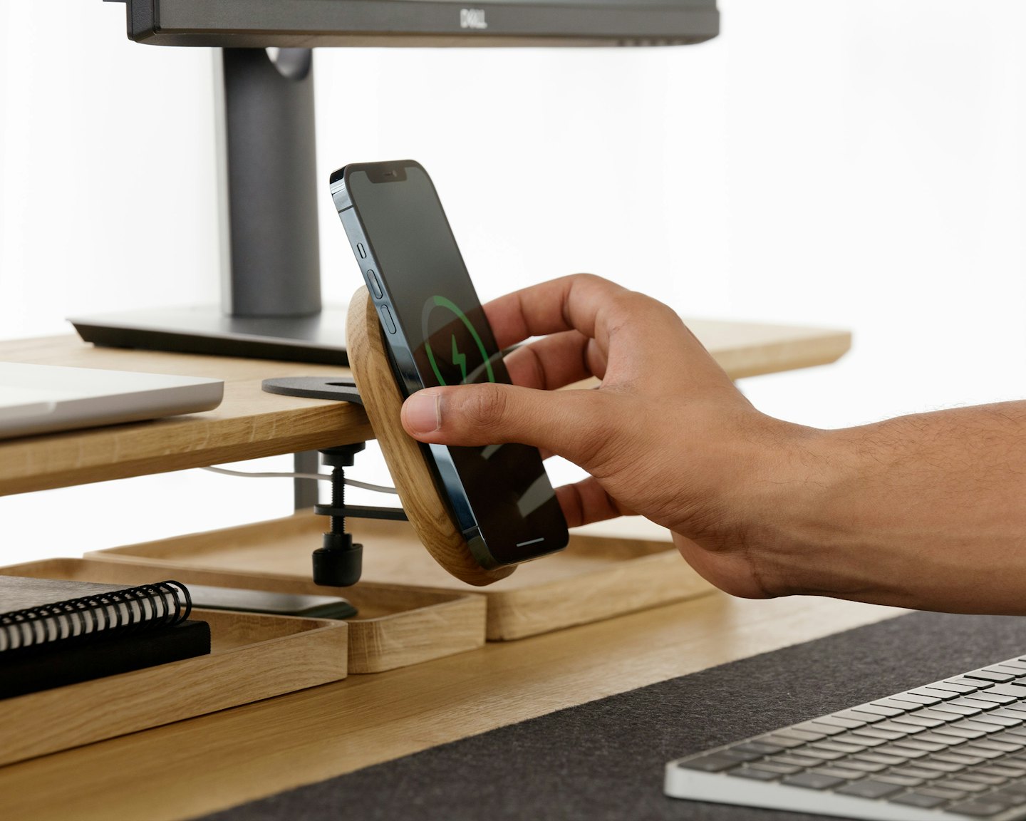 Una mano coloca un smartphone sobre un cargador inalámbrico de madera.