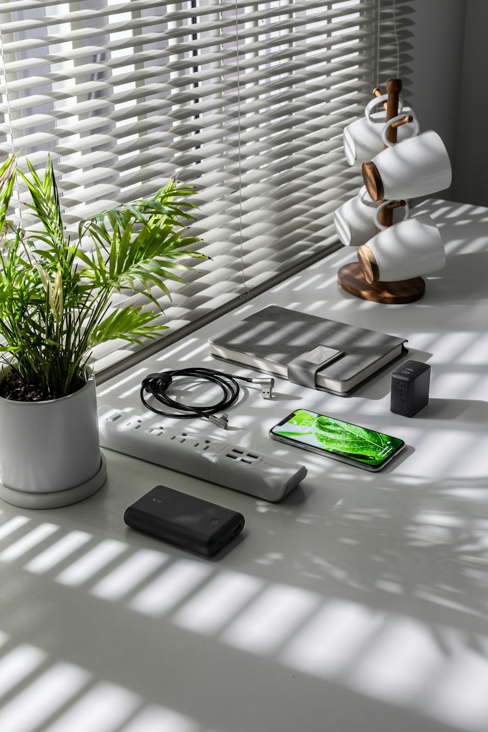 Escritorio con aparatos electrónicos, planta y tazas sobre un escritorio blanco.